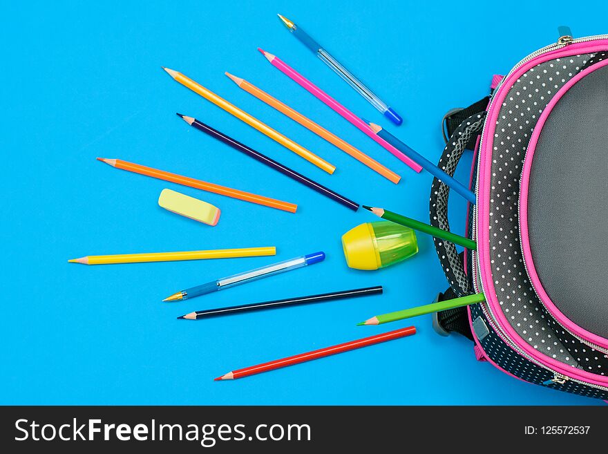 A lot of colored pencils and a school bag on blue background. Child`s school accessories. Flat lay. The view from the top. A lot of colored pencils and a school bag on blue background. Child`s school accessories. Flat lay. The view from the top.