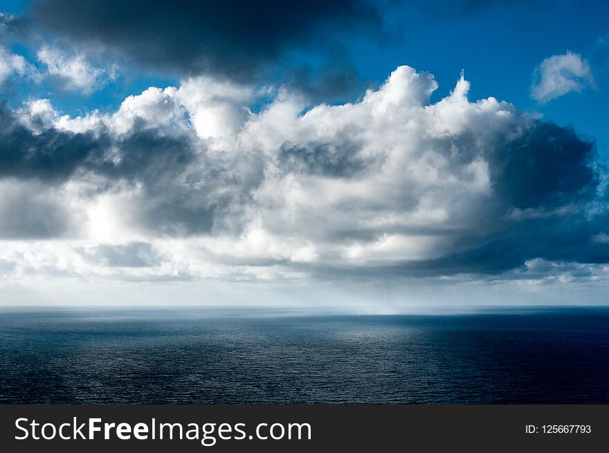 On a beautiful sunny day, gray, white and black clouds are playing over the sea and rain is falling in the distance. On a beautiful sunny day, gray, white and black clouds are playing over the sea and rain is falling in the distance