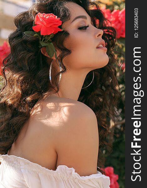 Girl with rose in dark curly hair and elegant white outfit