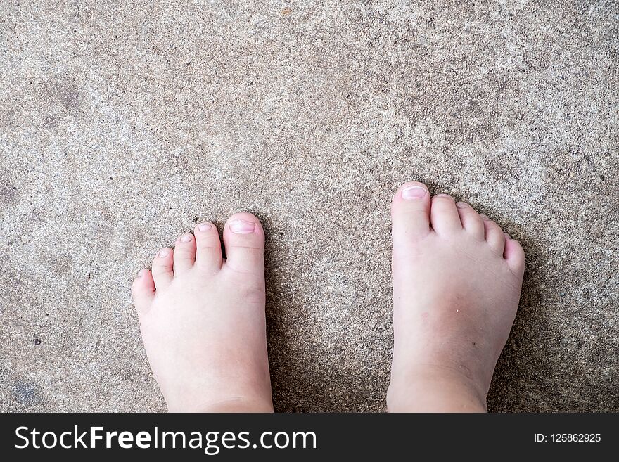 View from above of barefoot child with dirty feet standing on con