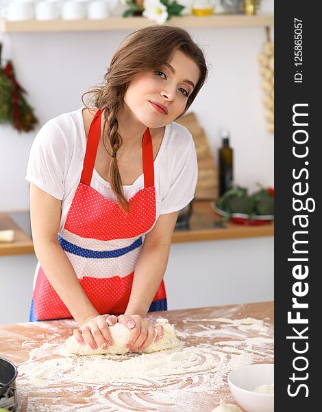 Young brunette woman cooking pizza or handmade pasta in the kitchen. Housewife preparing dough on wooden table. Dieting