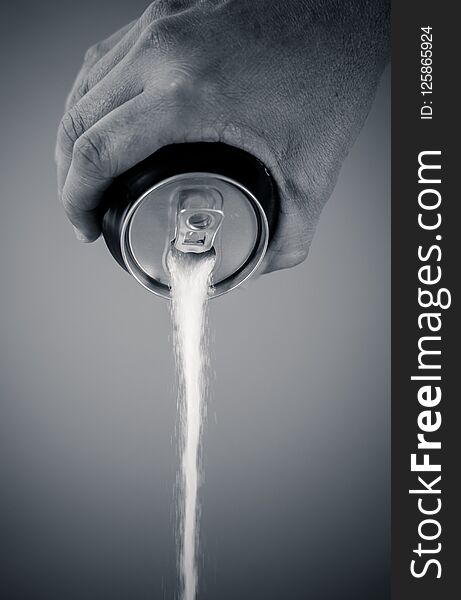 Black and withe portrait of a hand holding soda can pouring sugar in metaphor of sugar content of a refresh drink in healthy nutrition, diet, sweet and carbonated drinks addiction and unhealthy food concept. Black and withe portrait of a hand holding soda can pouring sugar in metaphor of sugar content of a refresh drink in healthy nutrition, diet, sweet and carbonated drinks addiction and unhealthy food concept.