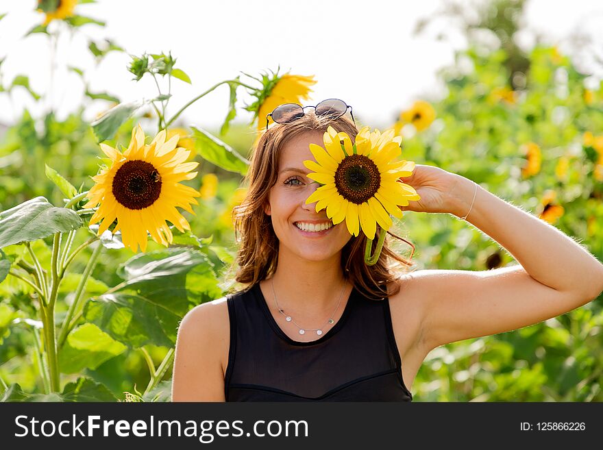 Laughing young woman holds a sunflower in front of her eyes.