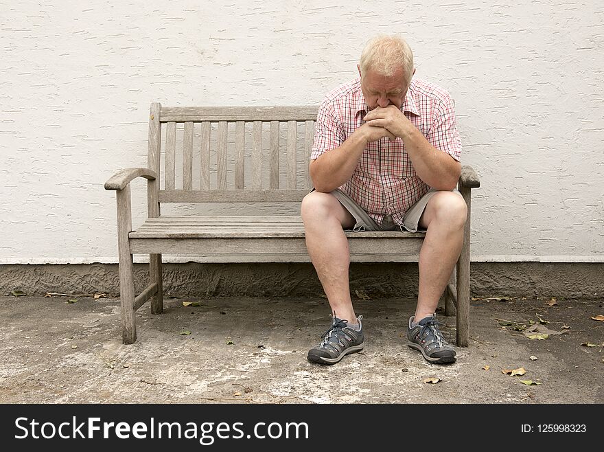 Upset Mature Man Sitting On A Wooden Bench