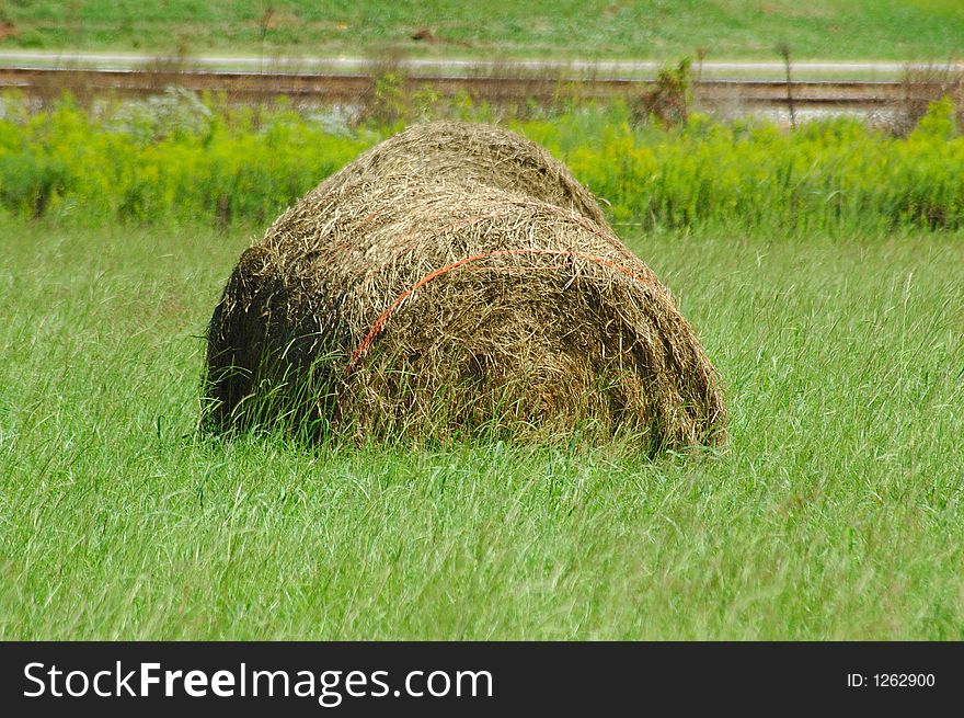 Bale of hay in a meadow or field near a railroad track. Bale of hay in a meadow or field near a railroad track