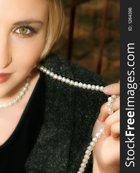 Blond woman with short hair playfully holding a string of pearls ? strong eye-contact. Blond woman with short hair playfully holding a string of pearls ? strong eye-contact