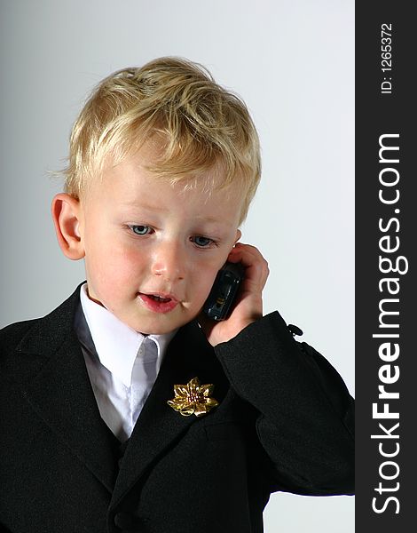 Toddler boy dressed up in black suit and white shirt talking on a mobile phone. Toddler boy dressed up in black suit and white shirt talking on a mobile phone