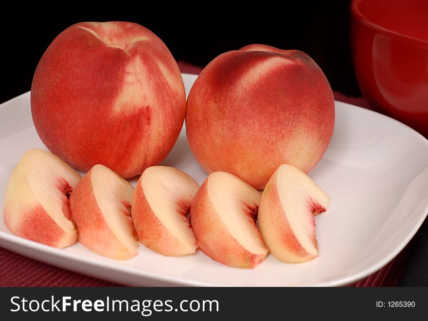Whole and sliced white peaches on a white plate on a burgundy placemat