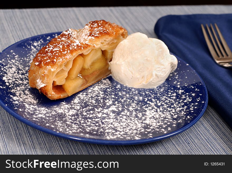 Apple strudel with vanilla ice cream on a blue plate dusted with powdered sugar