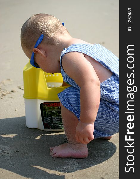 Toddler boy on the sand sticking his arm in a bait bucket