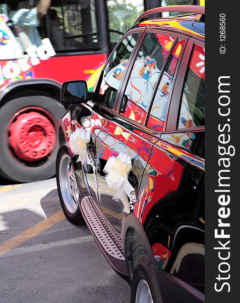 Colourful bus passing black wedding car with ribbons and reflections in the paint