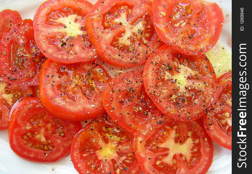 A plate of sliced tomatoes drizzled with olive oil and pepper. A plate of sliced tomatoes drizzled with olive oil and pepper