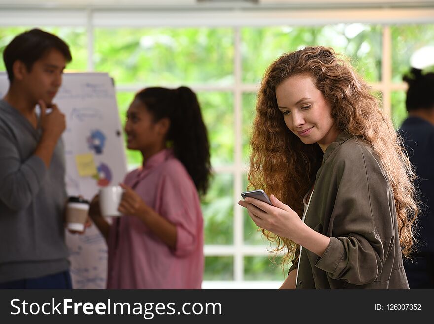 Young business woman using smartphone in the office with colleagues in the background