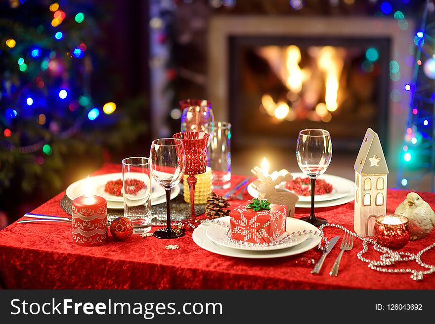 Beautiful table setting for Christmas party or New Year celebration at home. Cozy room with a fireplace and Christmas tree in a ba