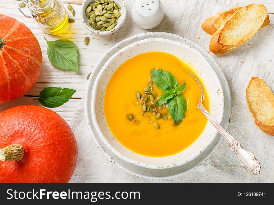 Dietary vegetarian pumpkin cream soup puree with olive oil, seeds and Basil on a light wooden table in a white plate. Selective focus