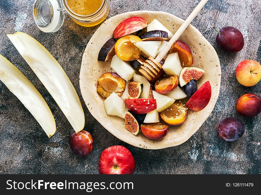 Fresh fruit salad of melon, figs, apples, plums and honey on a dark rustic background, top view. The concept of healthy eating. fl