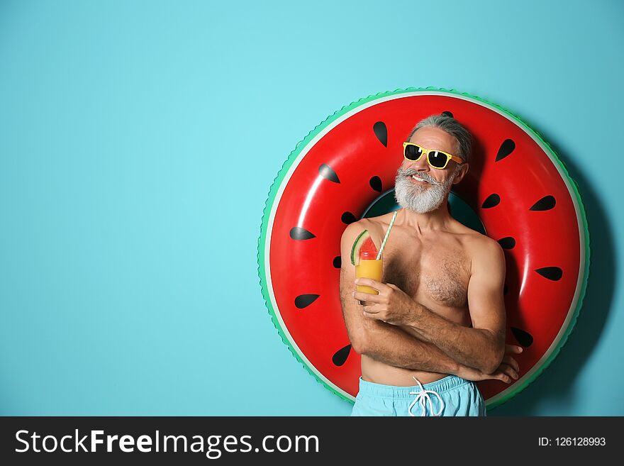 Shirtless man with inflatable ring and glass of cocktail on color background