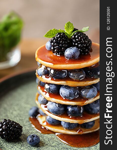 Tasty pancakes with berries and syrup on plate