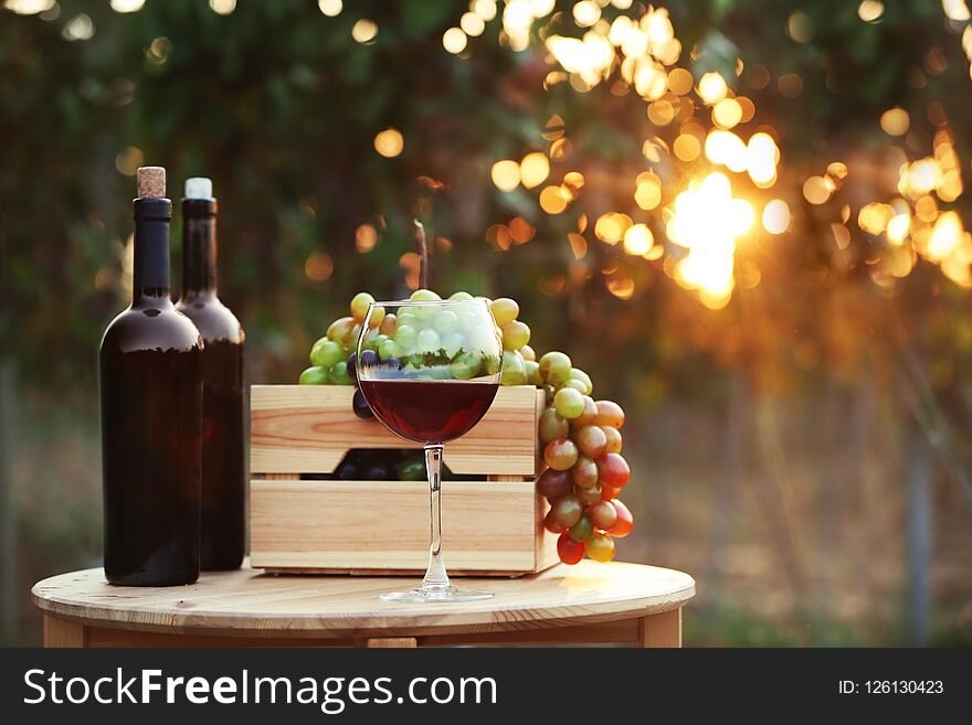 Bottles And Glass Of Red Wine With Fresh Grapes On Wooden Table