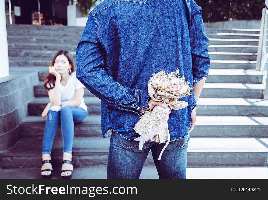 Handsome boyfriend is hiding bouquet of flower behind his back. Attractive handsome guy meet her today to make up with his beautiful girlfriend. His girlfriend is sulking and guy ask for apologize him