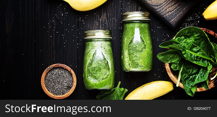 Incredibly useful green spinach smoothies in glass bottles with chia on wooden background with yellow bananas, top view