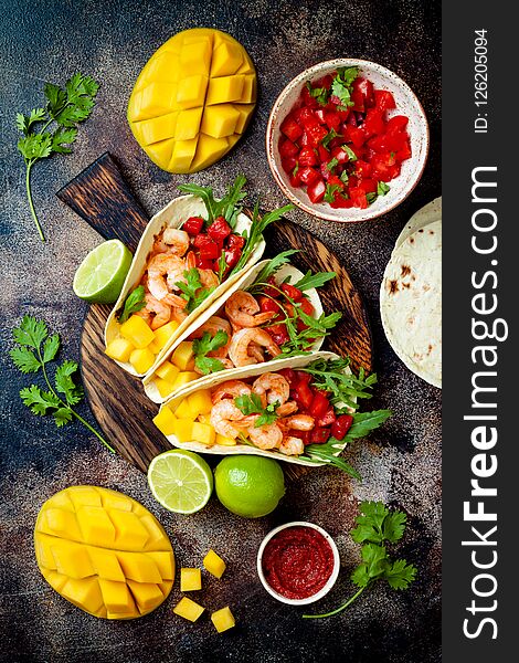 Mexican shrimp tacos with avocado, tomato, mango salsa on rustic stone table. Recipe for Cinco de Mayo party. Top view, overhead, flat lay.
