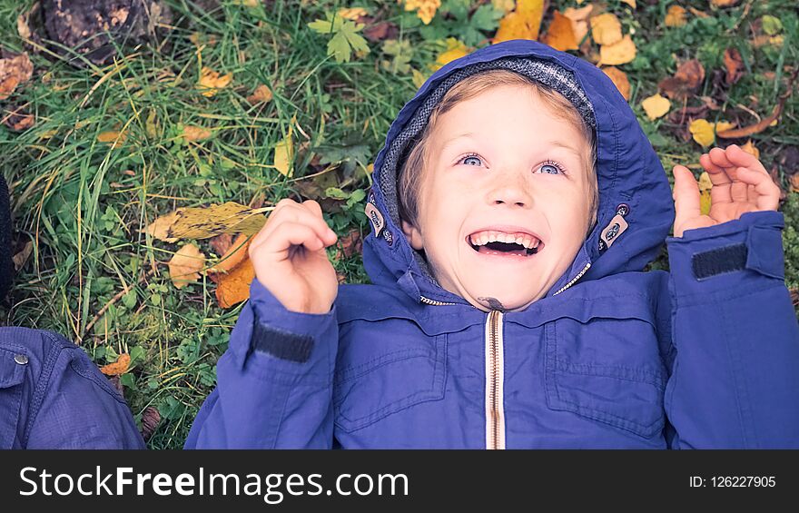 Little kid boy lying in autumn leaves in blue jacket. Happy child having fun in autumn park on warm day. Cute school boy