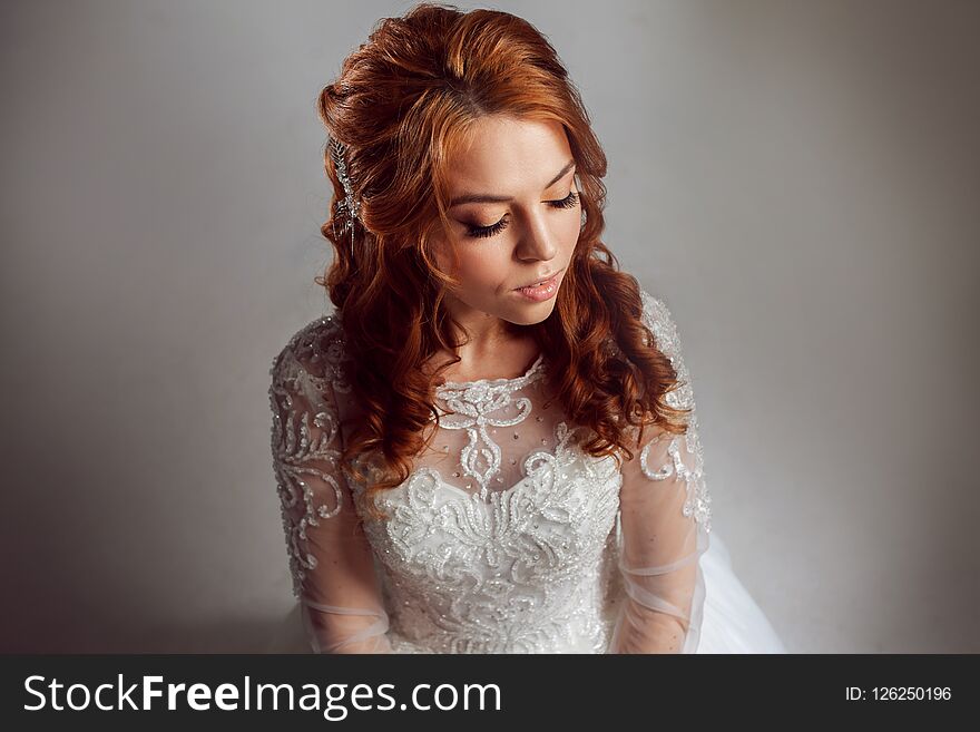Portrait of a charming red-haired bride, Studio, close-up. Wedding hairstyle and makeup. Young woman in luxurious wedding dress.