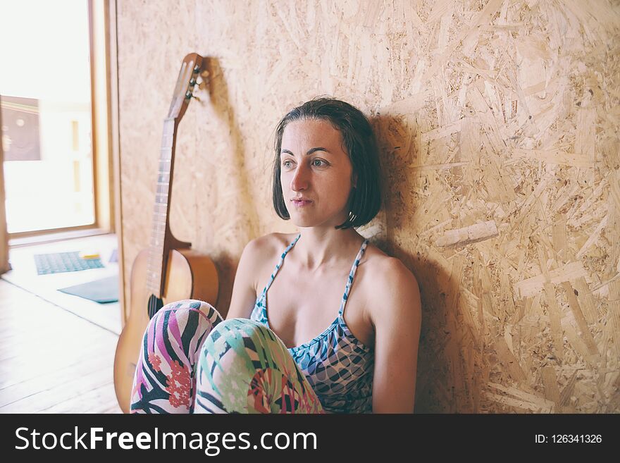 Thoughtful girl sits on the wooden floor next to the guitar. Acoustic guitar. Musician and musical instrument. Woman on the background of a wooden wall. Thoughtful girl sits on the wooden floor next to the guitar. Acoustic guitar. Musician and musical instrument. Woman on the background of a wooden wall.