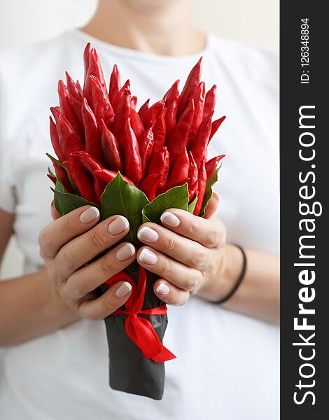 Woman is holding a small bouquet made of red hot peppers in the form of a heart