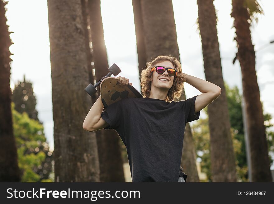 Stylish young blond curly hair man holding skateboard on shoulders and smile. Stylish young blond curly hair man holding skateboard on shoulders and smile