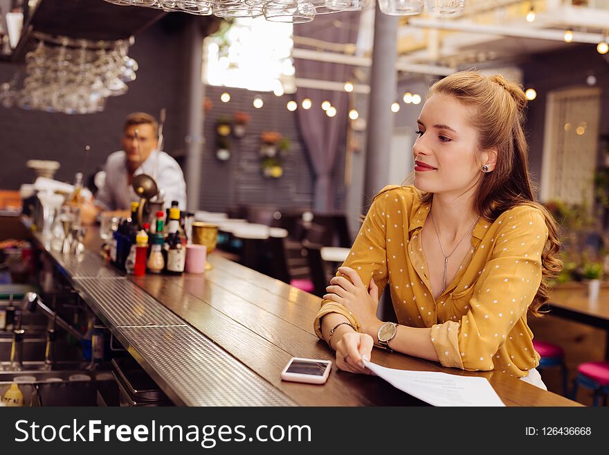 Relaxing alone. Calm beautiful young girl kindly smiling and looking at the professional barman while sitting opposite him. Relaxing alone. Calm beautiful young girl kindly smiling and looking at the professional barman while sitting opposite him