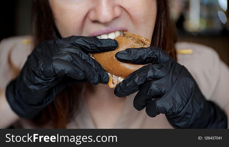 Close up of pretty girl in black gloves eating a hamburger in cafe