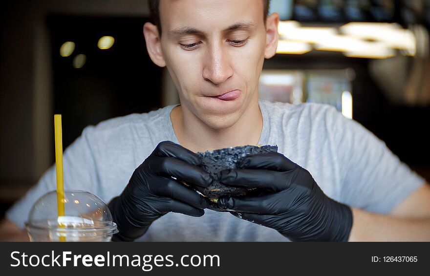 A young man sits in a restaurant and looks carefully at the burger who holds in his hands