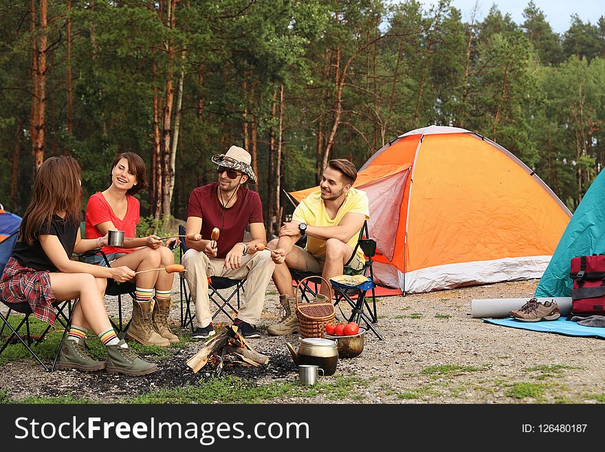 People having lunch with sausages near camping tent outdoors