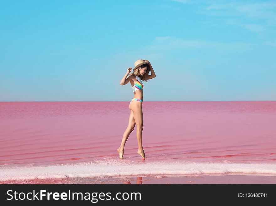 Beautiful woman in swimsuit standing near pink lake