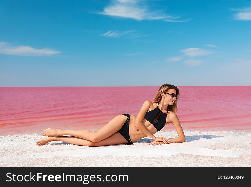 Beautiful woman in swimsuit lying near pink lake on sunny day