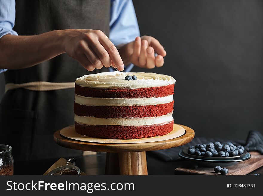 Woman decorating delicious homemade red velvet cake with blueberries at table