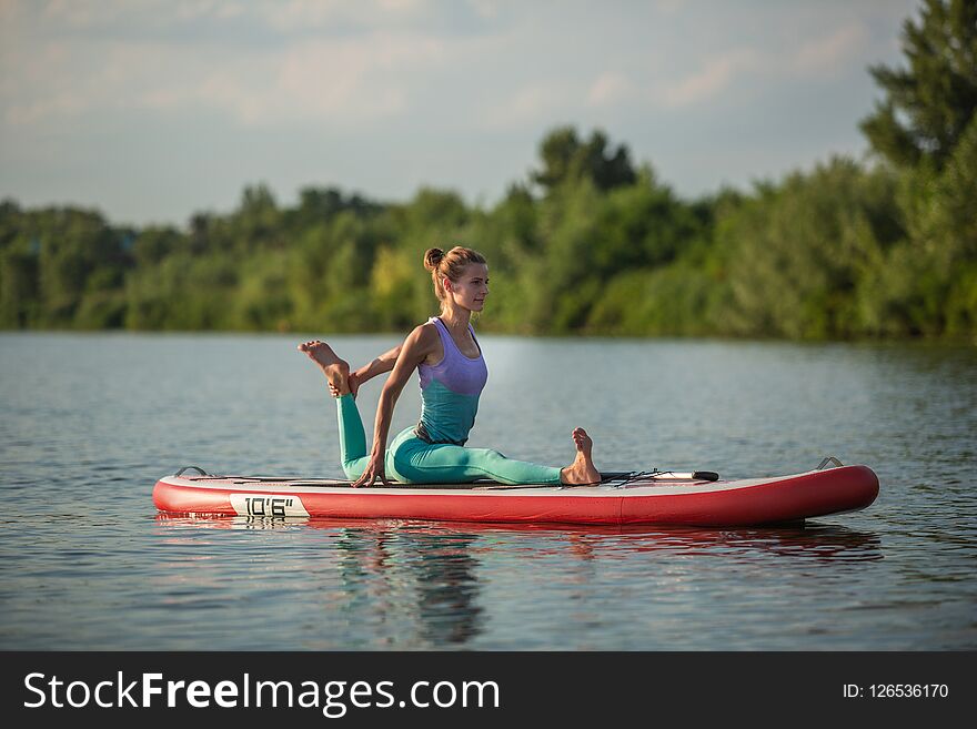 Young woman doing yoga on sup board with paddle. Meditative pose, side view - concept of harmony with the nature