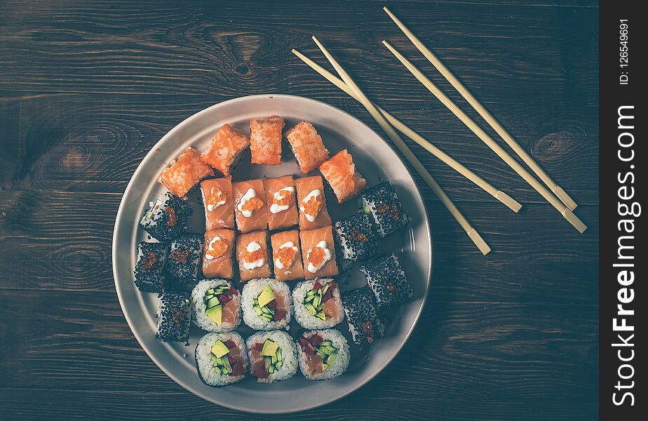 Sushi Set rolls and sashimi served in traditional round plate. On wooden background with sticks. Sushi Set rolls and sashimi served in traditional round plate. On wooden background with sticks