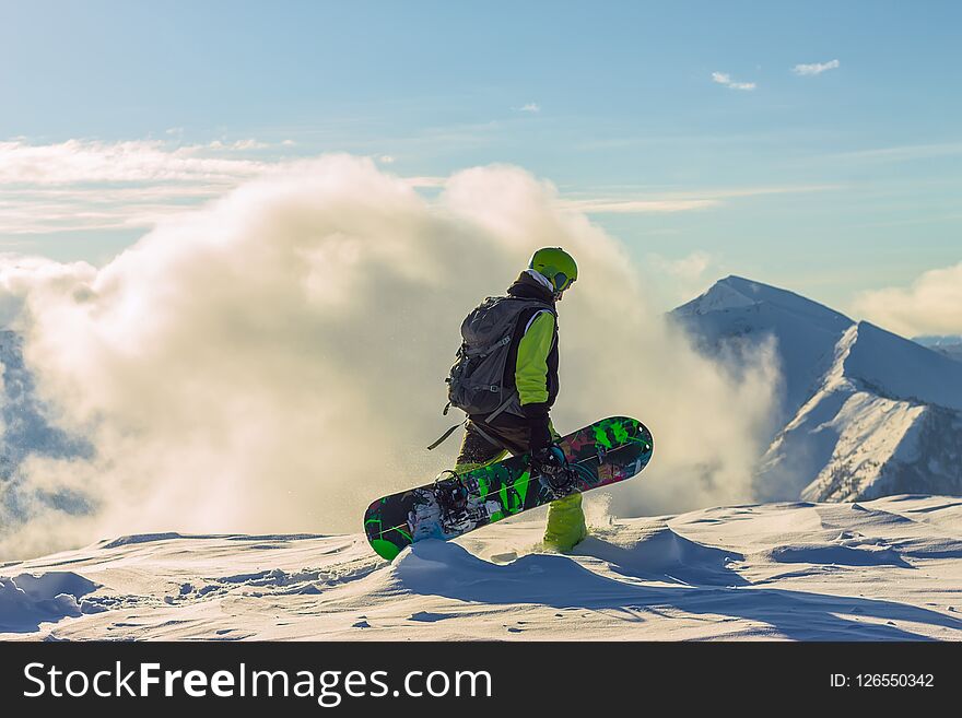 Snowboarder freerider is standing in the snowy mountains in winter under the clouds.