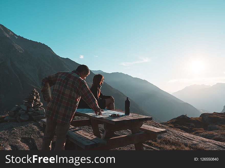 Coouple hikers reading trekking map on table in backlight, rear view. Adventure exploration on the Alps.