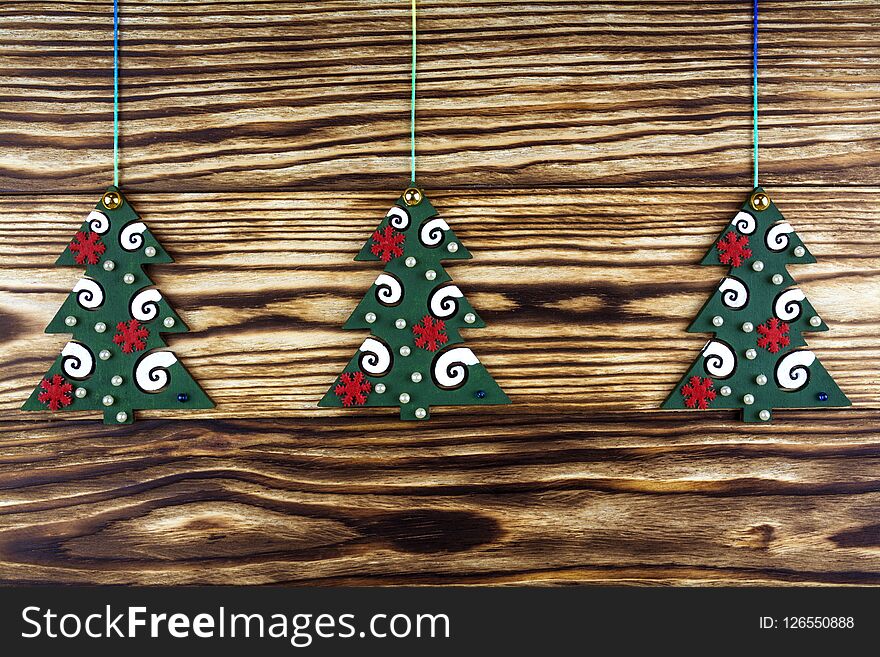 Three Toy Green Fir Trees With Decorative Ornaments On A Wooden Background.