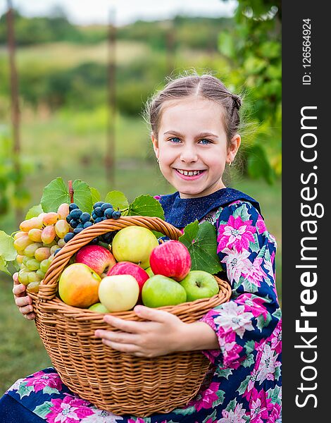 A little girl with a basket, with red apples and grapes in the garden. A little girl with a basket, with red apples and grapes in the garden.