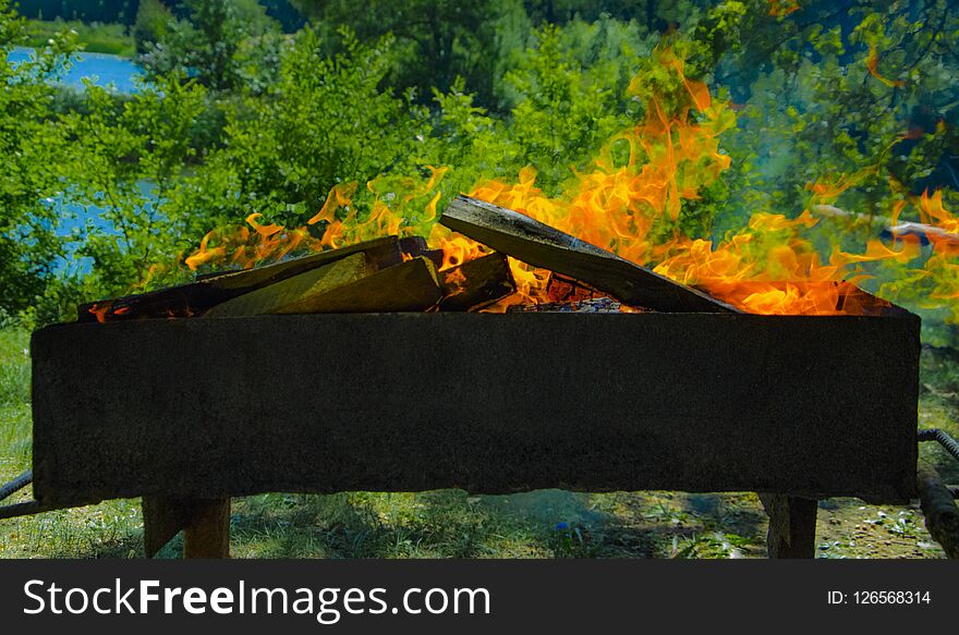 A roaster with burning coals and a red flame Burned firewood in the grill.