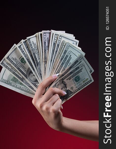 Woman hand hand with beautiful manicure holding fan of dollars, closeup shot on dark red background. Woman hand hand with beautiful manicure holding fan of dollars, closeup shot on dark red background