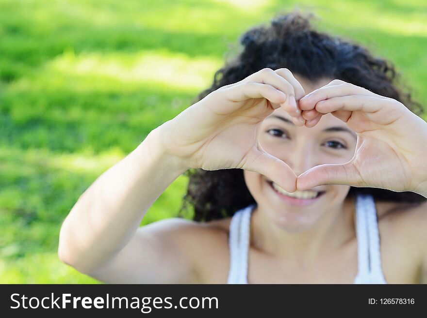 Close up focus woman hands show love symbol on green nature outdoor park. Young latin girl. Close up focus woman hands show love symbol on green nature outdoor park. Young latin girl.