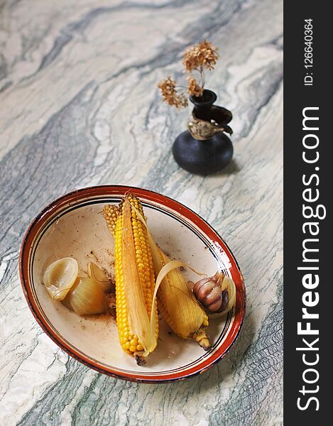 A plate with cobs of boiled corn, standing on a stone table. A plate with cobs of boiled corn, standing on a stone table