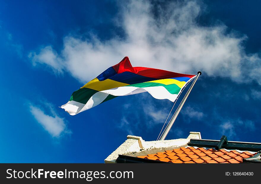 Waving flag of Wadden Island Terschelling on top of roof with red roof tiles against a blue sky with white clouds. Waving flag of Wadden Island Terschelling on top of roof with red roof tiles against a blue sky with white clouds