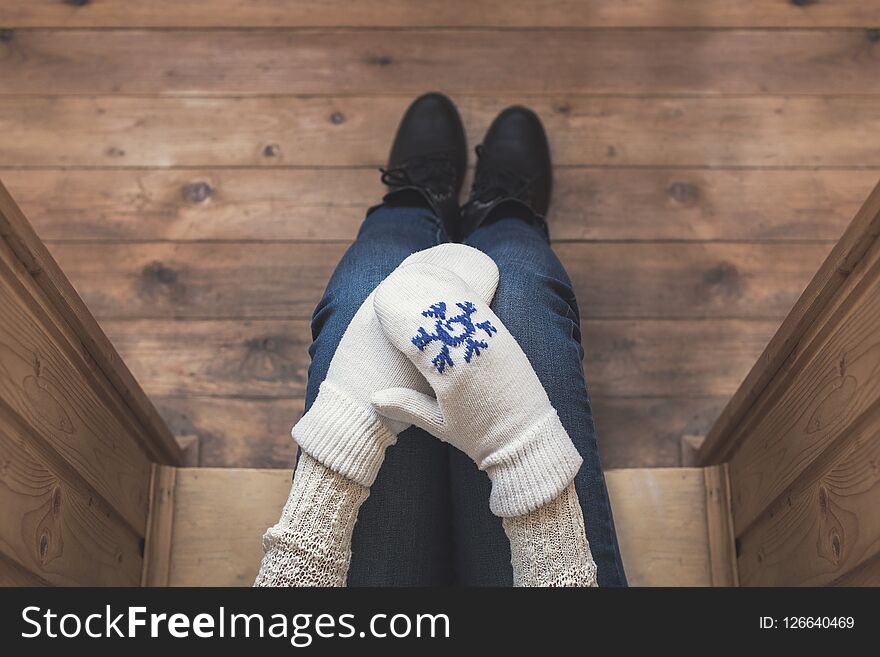 A girl in the winter knitted mittens with an iron mug of coffee on the terrace of a wooden house.